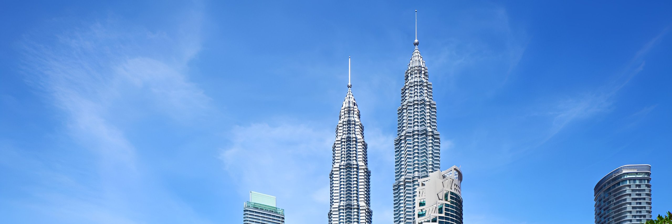 Panoramic skyline with twin silver skyscrapers and modern buildings beneath a bright blue sky.